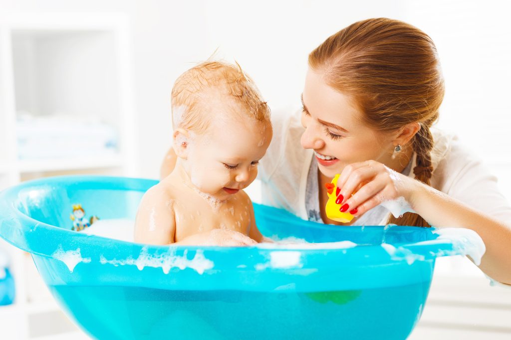 Happy family mother bathes the baby in a blue bath