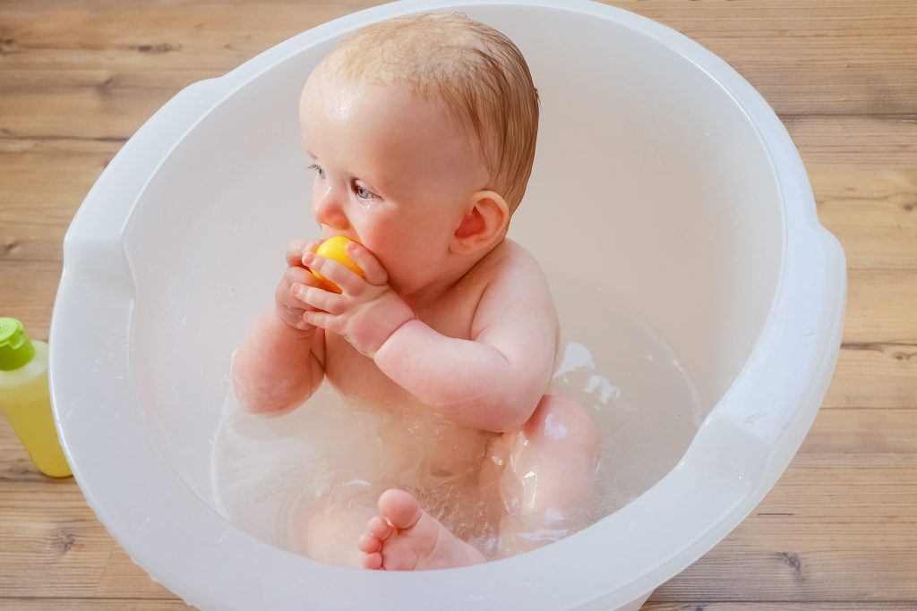 Pensive cute wet baby biting yellow rubber toy