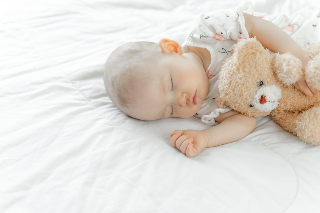 The newborn baby slept on a white bed and hugged the bear.