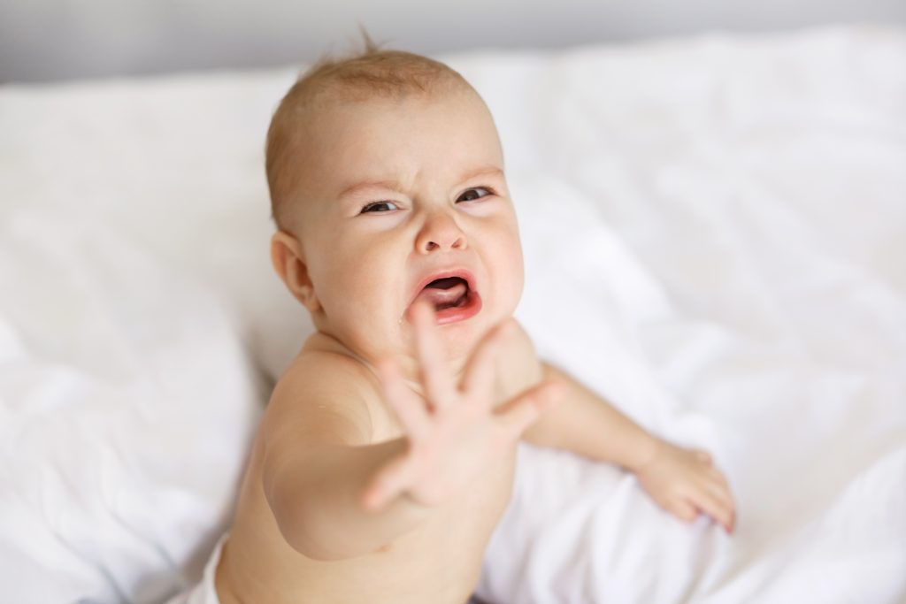 Cute nice little baby girl crying lying with her mom on bed at home.